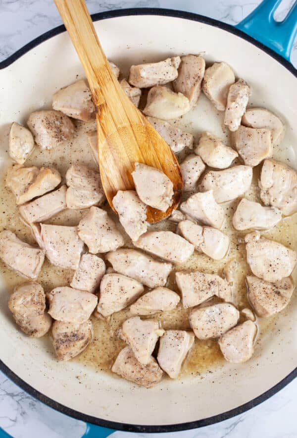 Diced chicken breasts sauteed in skillet with wooden spoon.