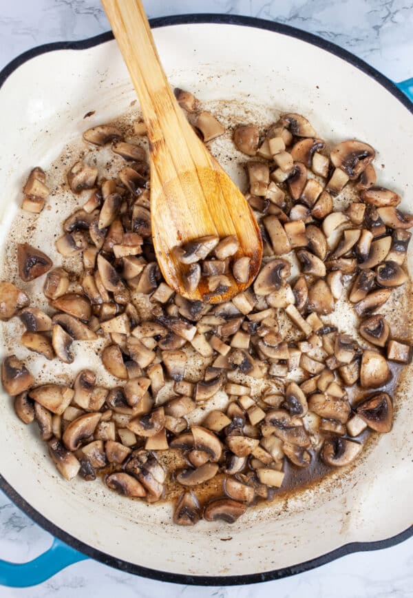 Chopped mushrooms sauteed in skillet with wooden spoon.