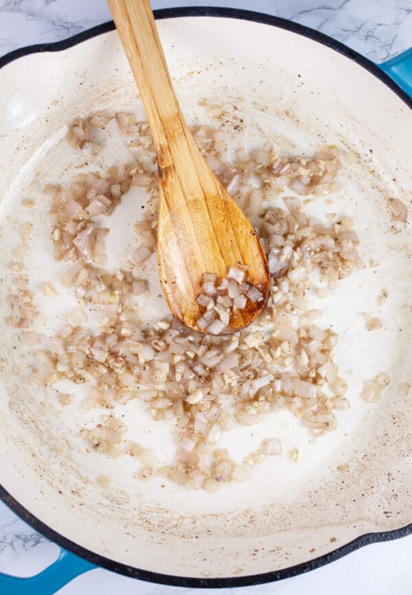 Minced garlic and shallots sauteed in skillet with wooden spoon.
