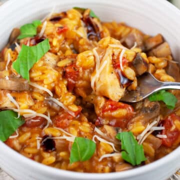 Chicken mushroom tomato pasta garnished with fresh basil and balsamic glaze in white bowl with fork.