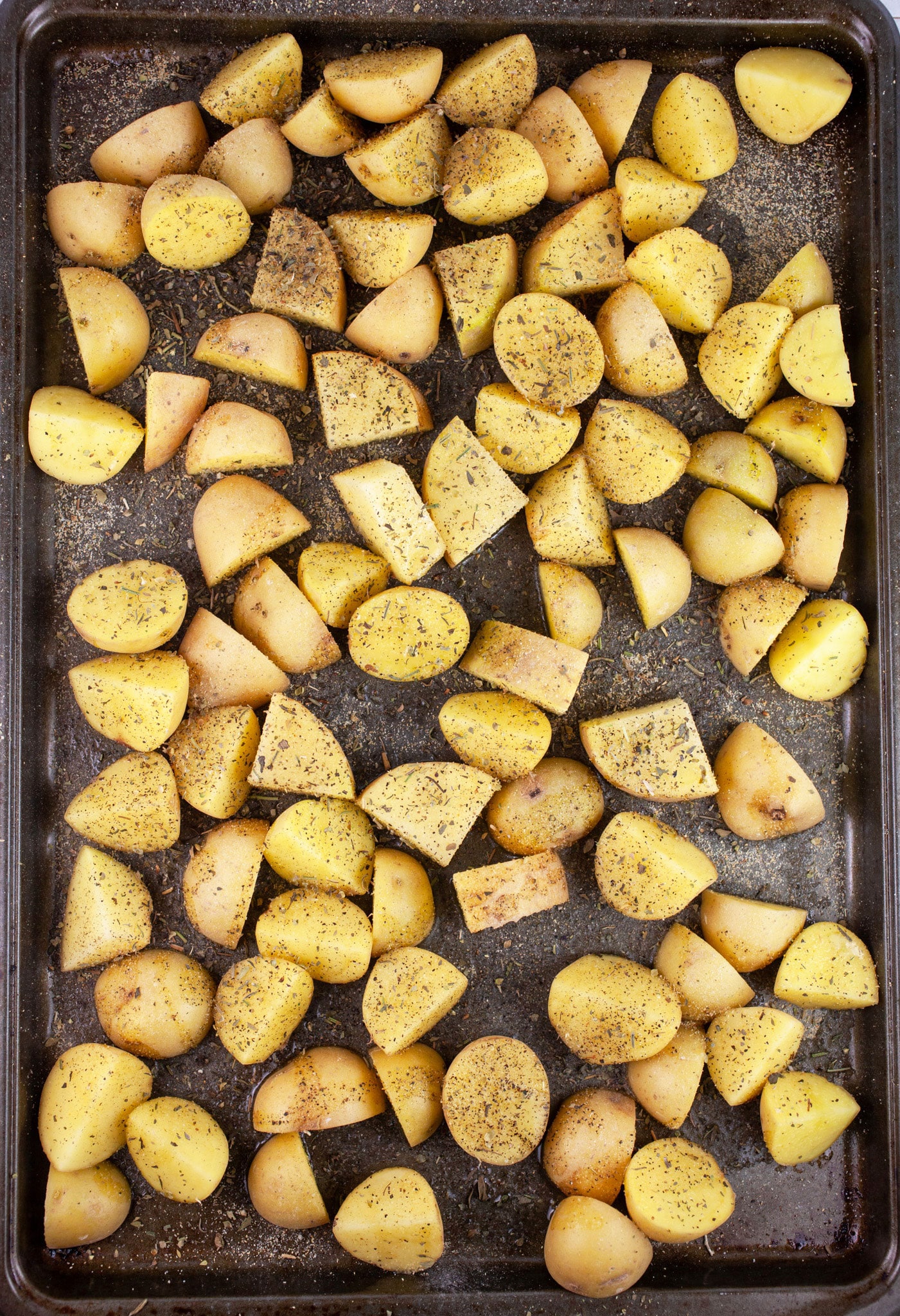 Uncooked, diced Yukon gold potatoes tossed in olive oil and spices on baking sheet.