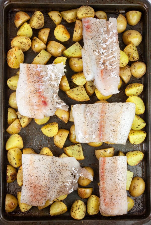 Uncooked cod filets on top of roasted potatoes on baking sheet.