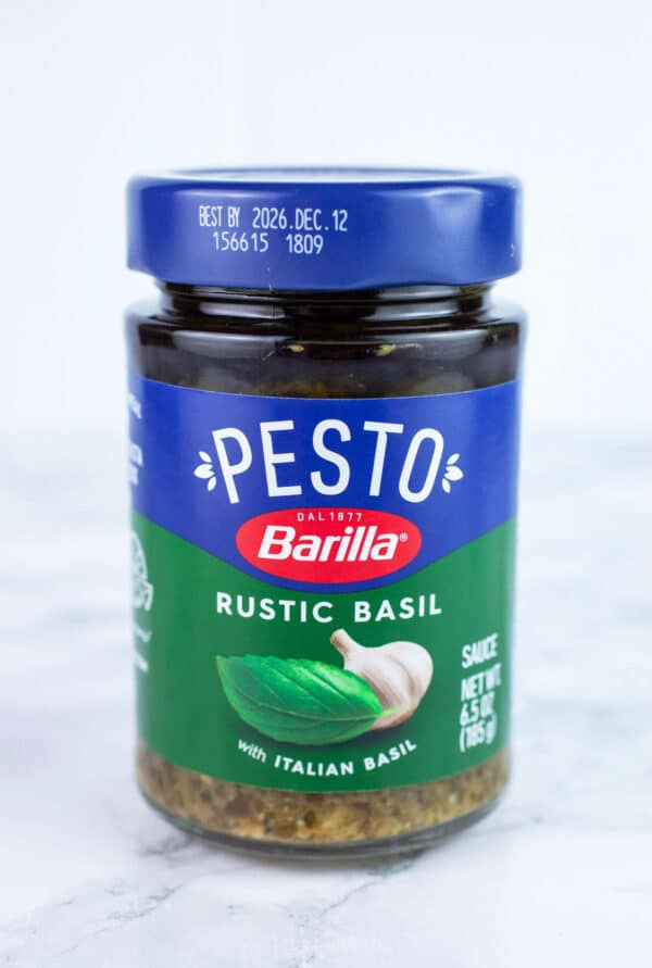 Unopened jar of basil pesto on white surface.