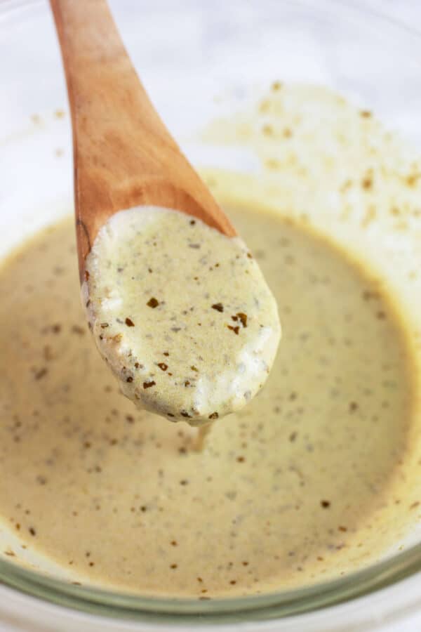 Basil pesto mayo sauce lifted from glass bowl on wooden spoon.