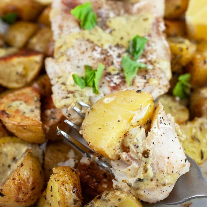Pesto baked cod and potatoes with fork garnished with fresh basil.