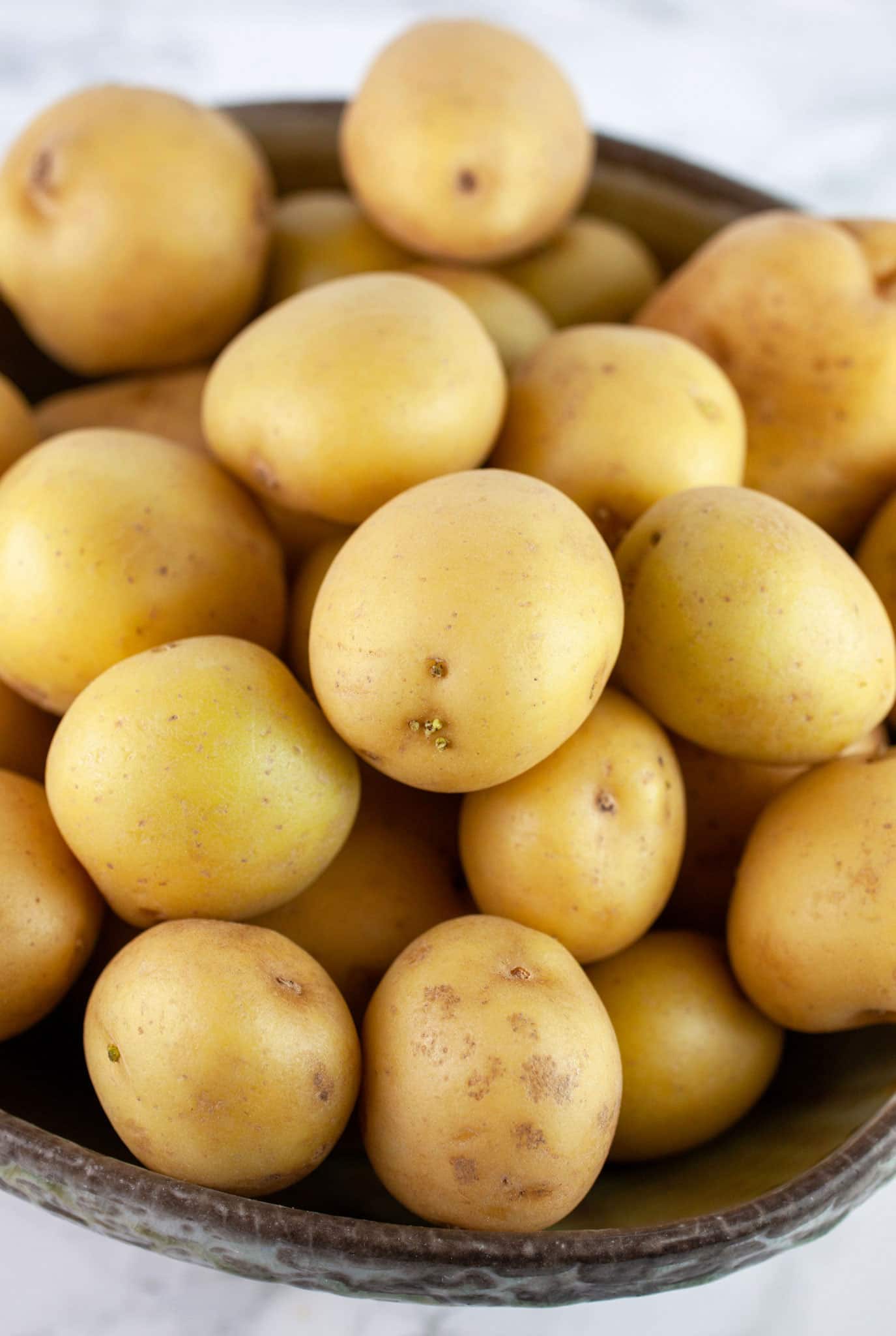 Whole, unpeeled Yukon gold potatoes in ceramic bowl.