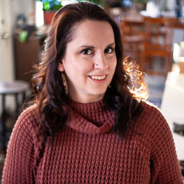 Brunette woman in kitchen wearing burgundy sweater.