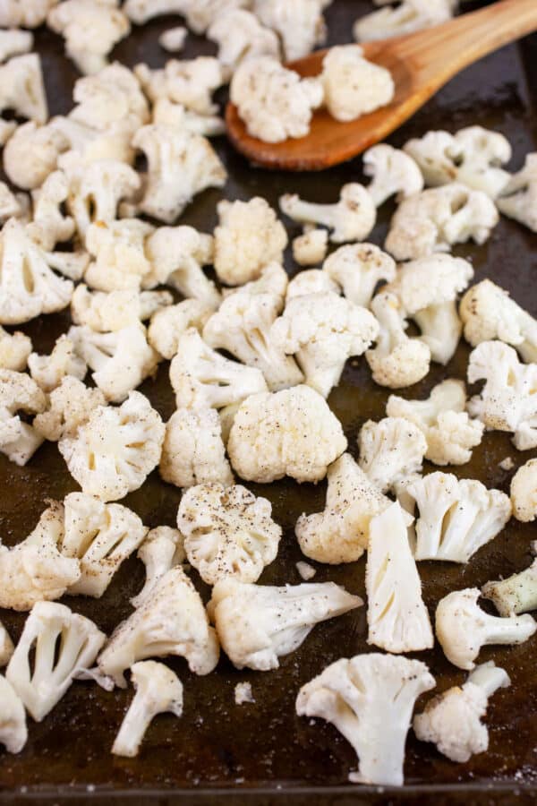 Uncooked cauliflower florets on baking sheet with wooden spoon.