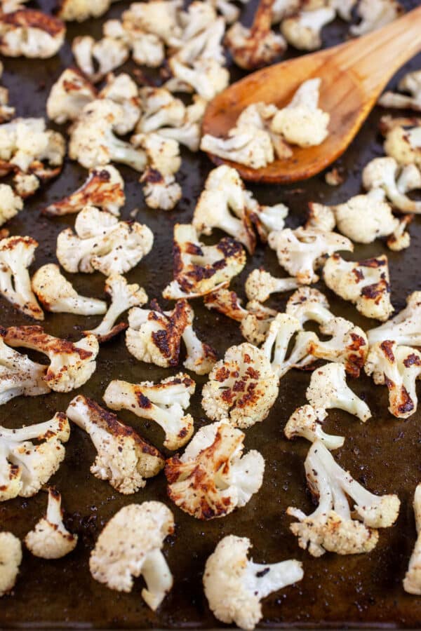 Roasted cauliflower florets on baking sheet with wooden spoon.