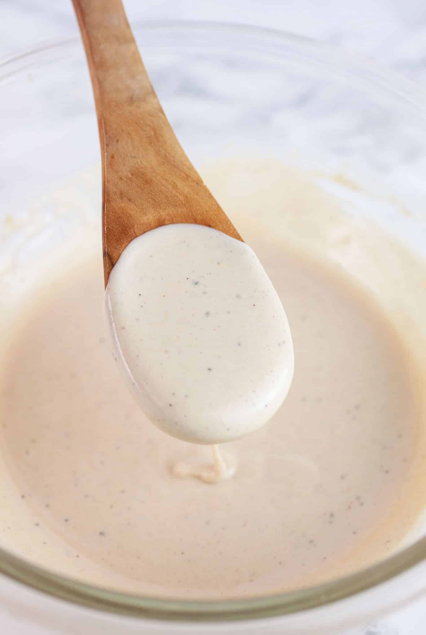Wooden spoonful of lemon tahini sauce lifted from glass bowl.