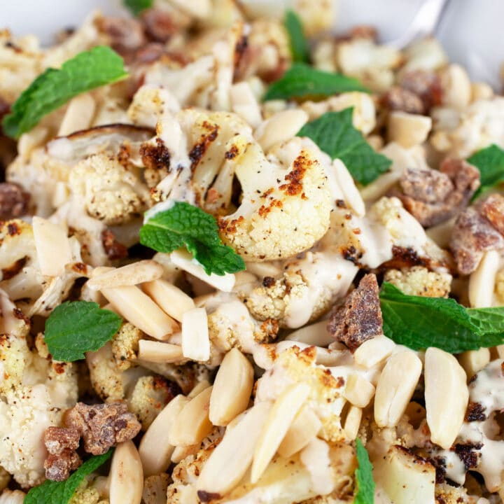 Mediterranean roasted cauliflower with slivered almonds, chopped dates, and fresh mint in white bowl with fork.