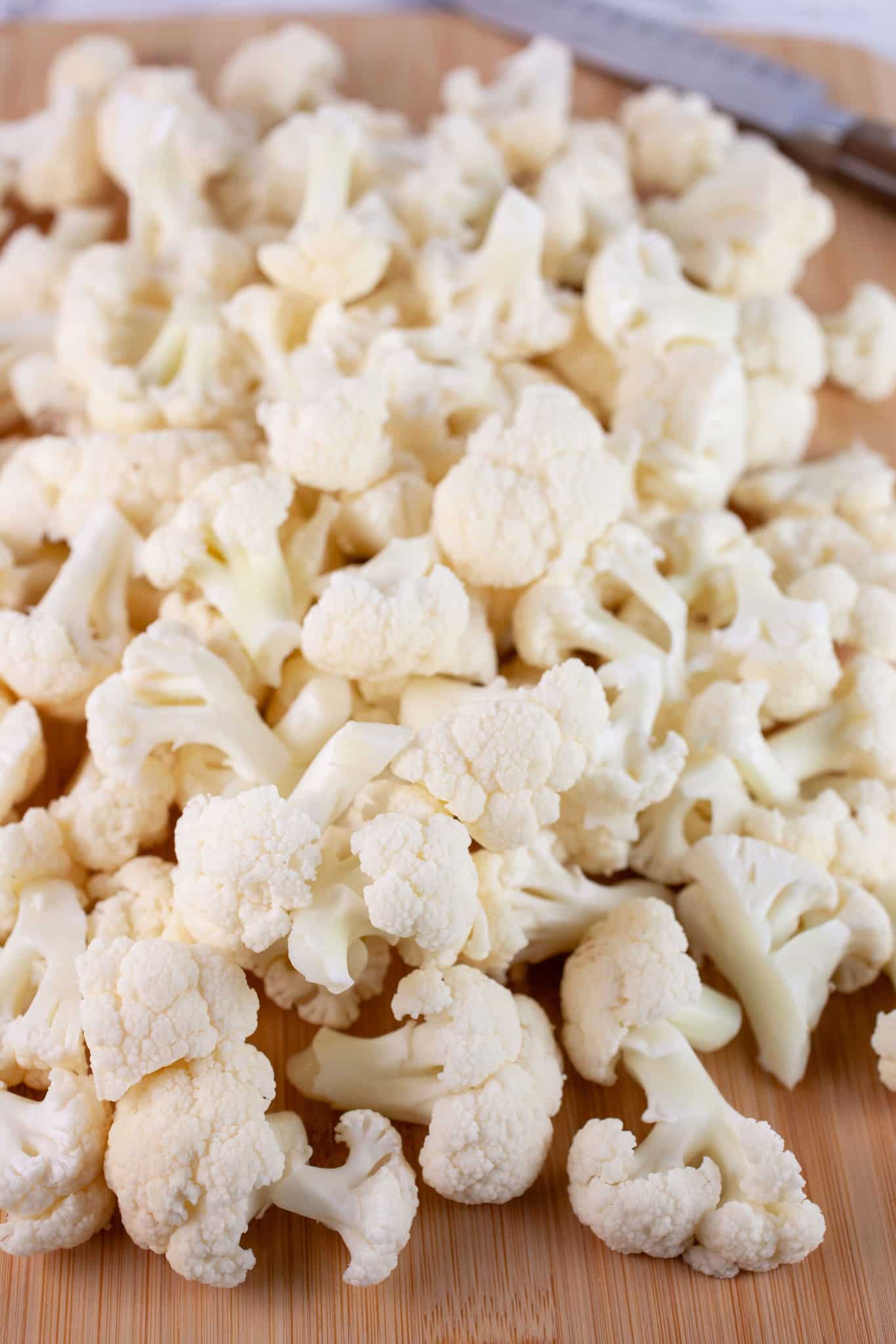 Cauliflower florets on wooden cutting board with knife.