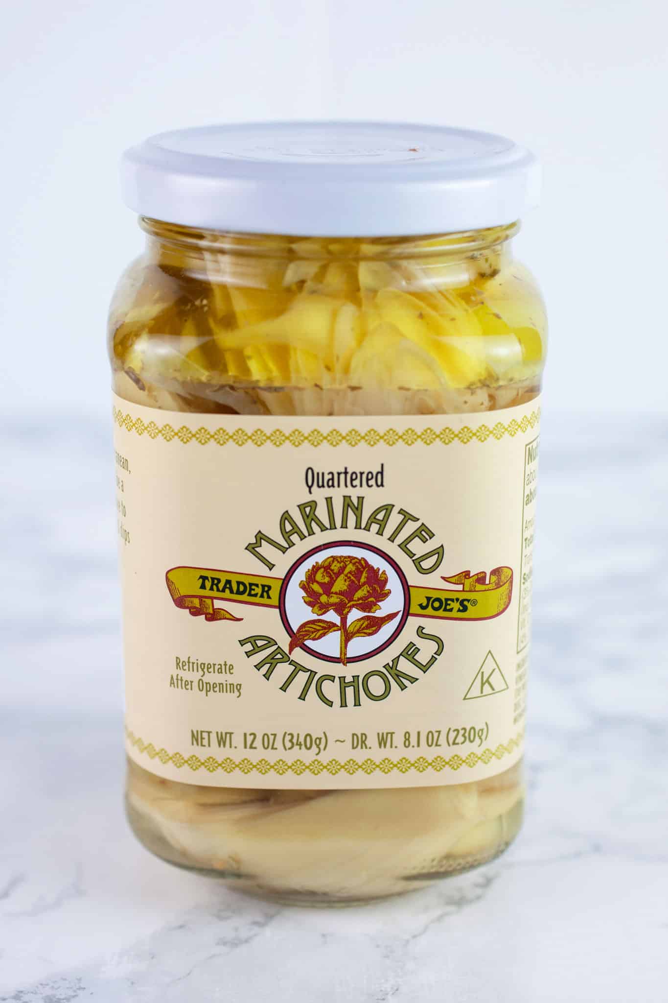 Unopened jar of marinated artichokes on white surface.
