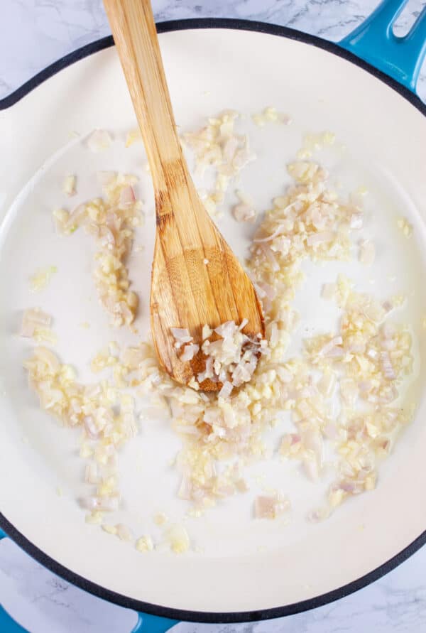 Minced garlic and onions sauteed in skillet with wooden spoon.