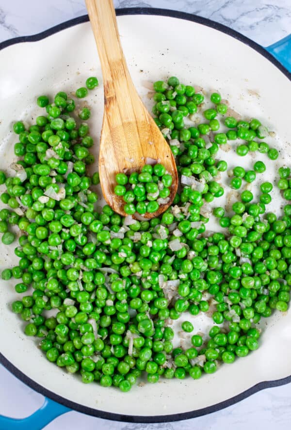 Minced garlic, shallots, and frozen peas sauteed in skillet with wooden spoon.