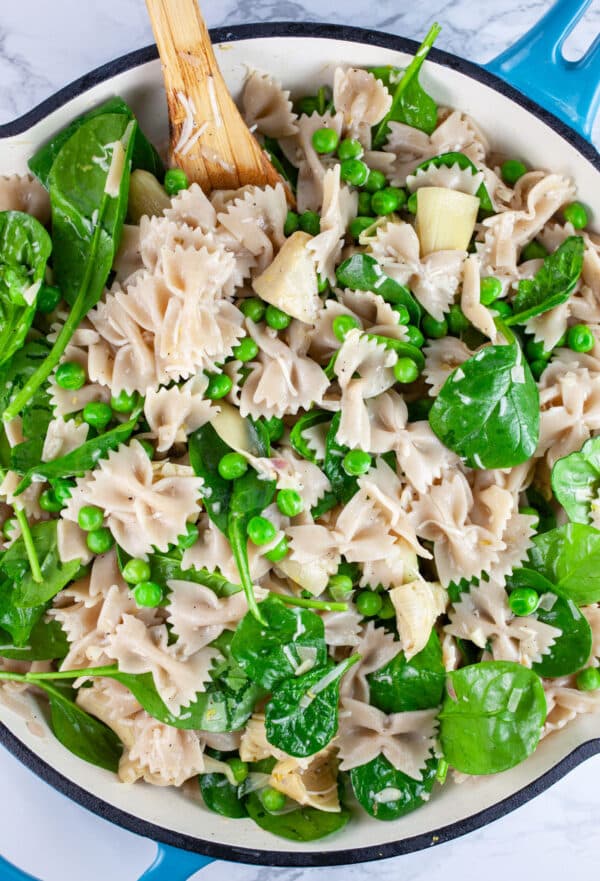 Spring vegetable pasta in skillet with wooden spoon.