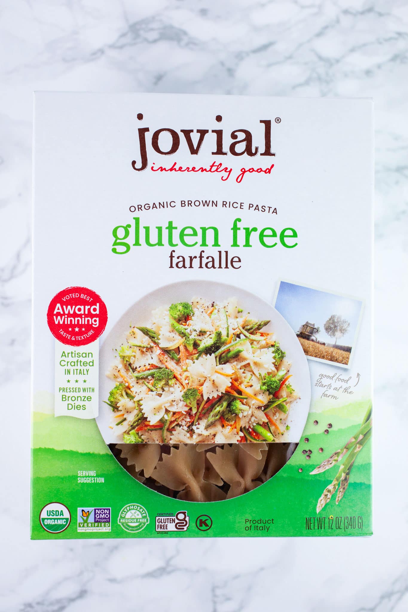 Unopened box of gluten free farfalle pasta on white surface.