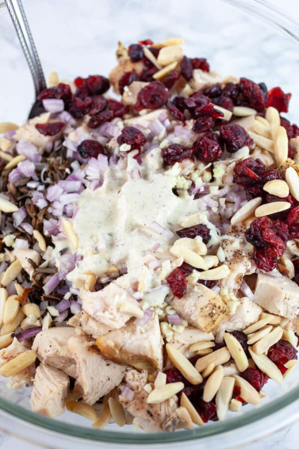 Diced chicken, wild rice, dried cranberries, slivered almonds, and dressing in glass bowl with spoon.