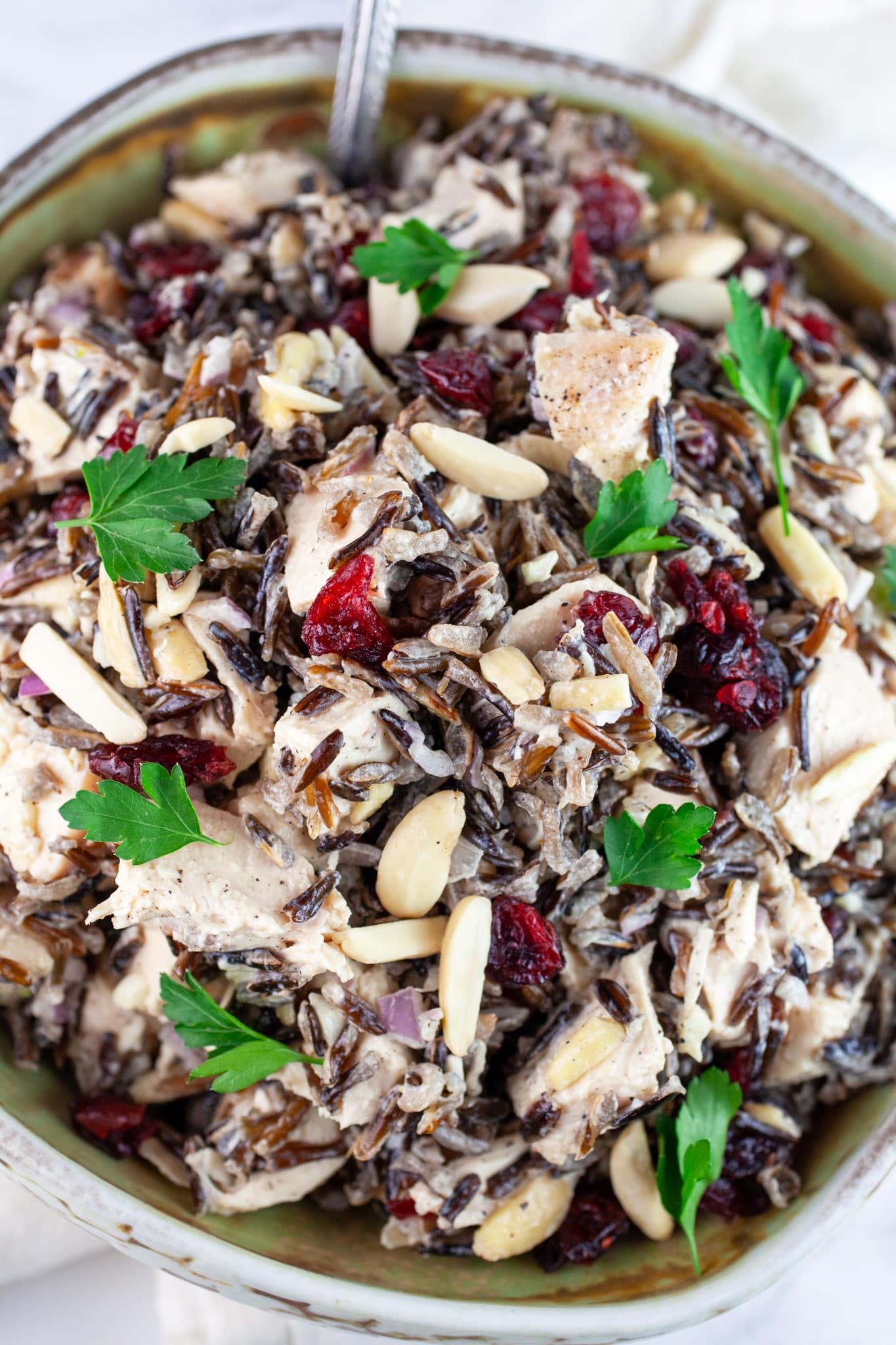 Wild rice chicken salad in ceramic bowl with spoon garnished with fresh parsley.