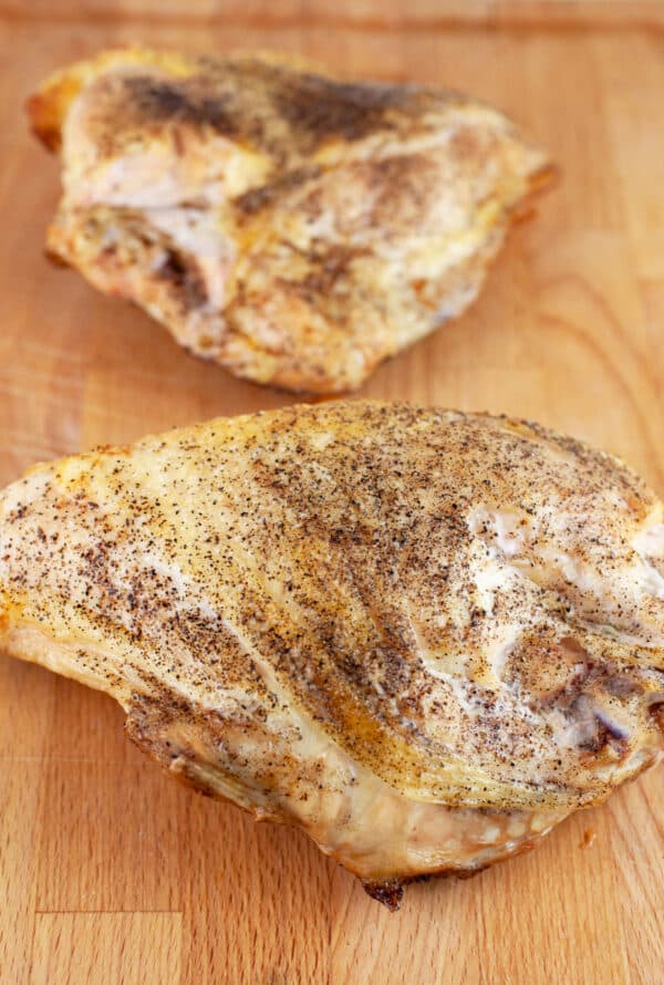Roasted split chicken breasts on wooden cutting board.