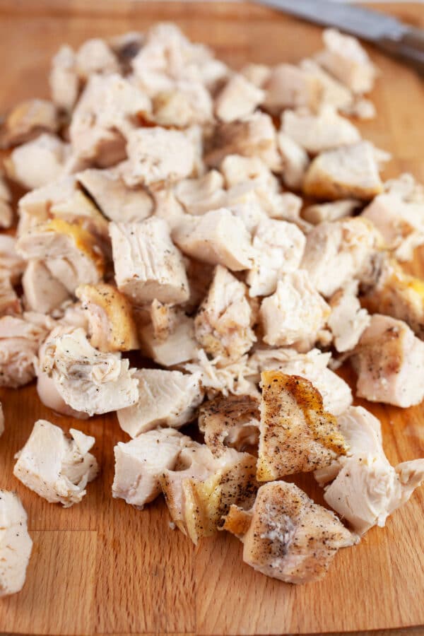 Diced roasted split chicken breasts on wooden cutting board with knife.