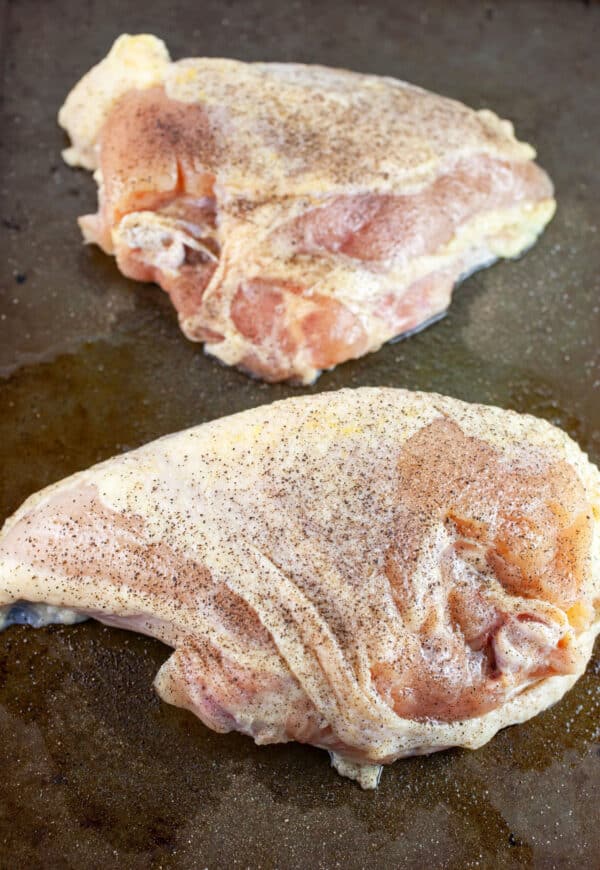Raw split chicken breasts with olive oil, kosher salt and pepper on baking sheet.