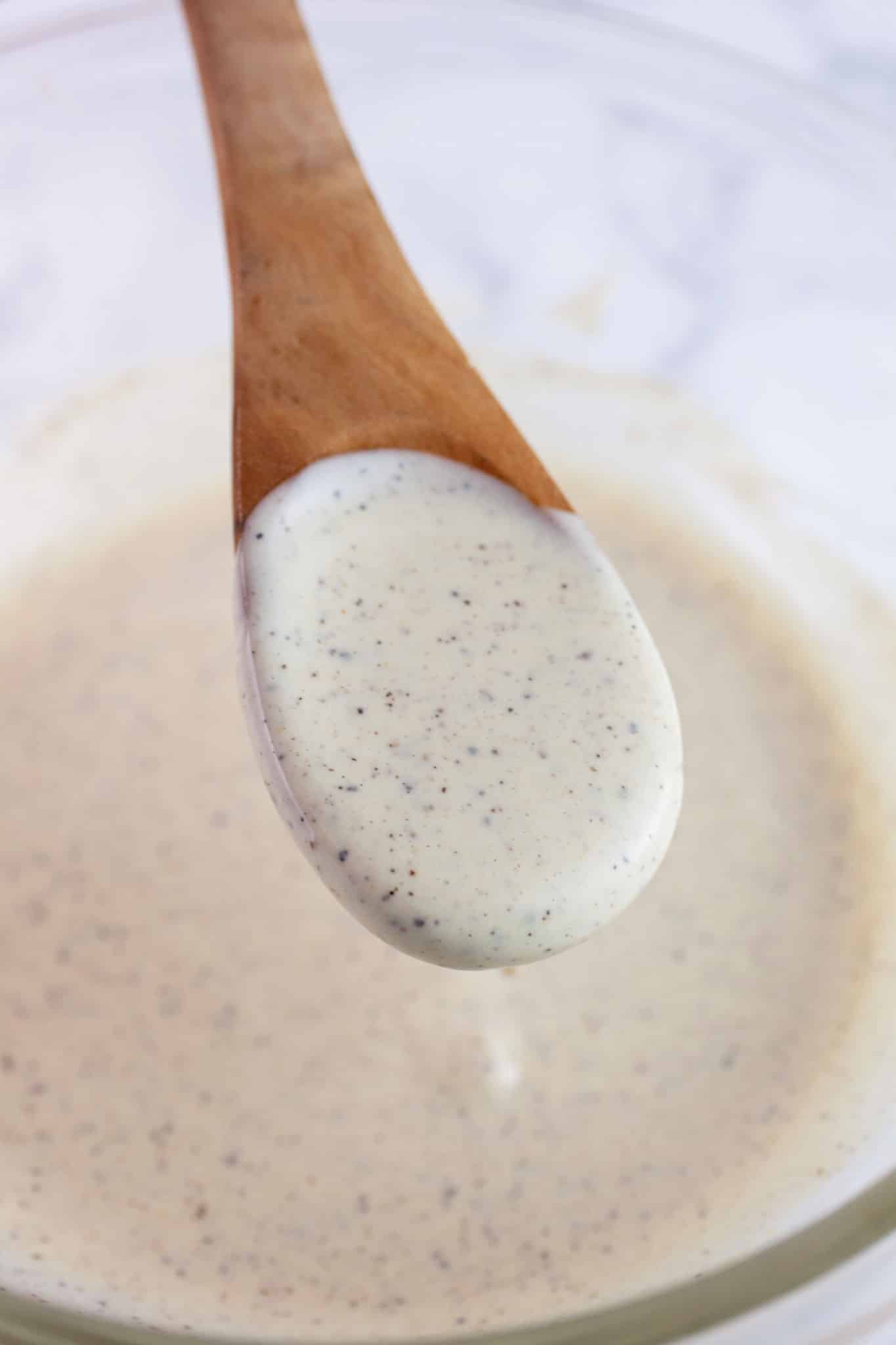 Wooden spoonful of mayo Dijon dressing lifted from small glass bowl.