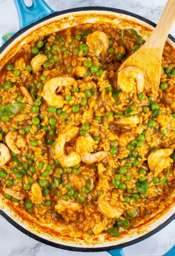 Curry orzo pasta with peas and shrimp in skillet with wooden spatula.