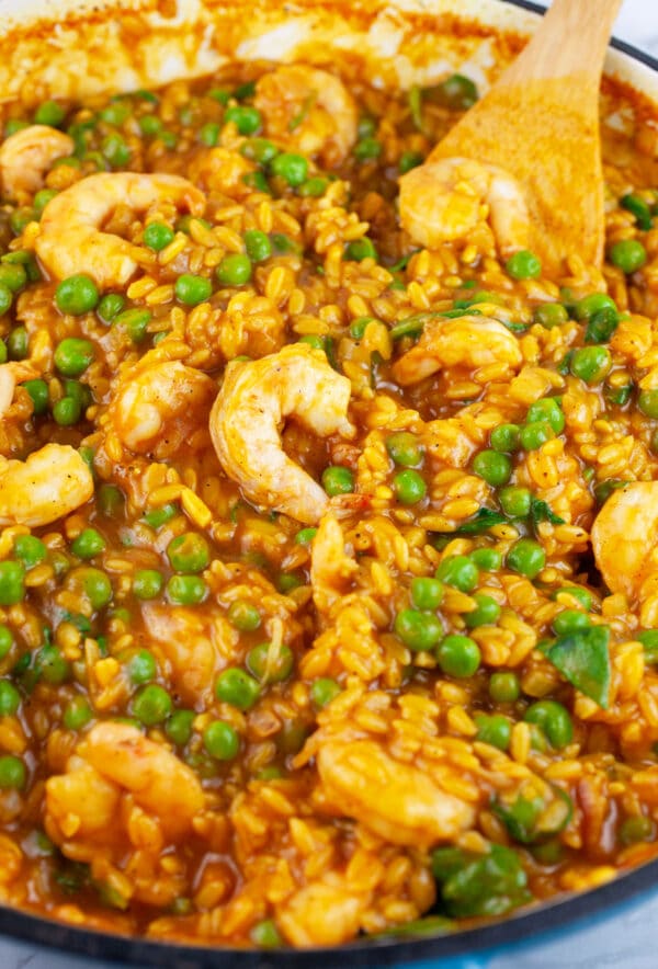 Curried orzo pasta with peas and shrimp in skillet with wooden spatula.