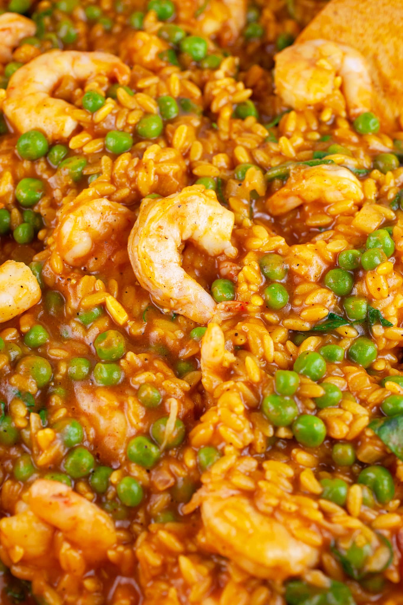 Curry orzo pasta with peas, spinach, and shrimp in skillet.