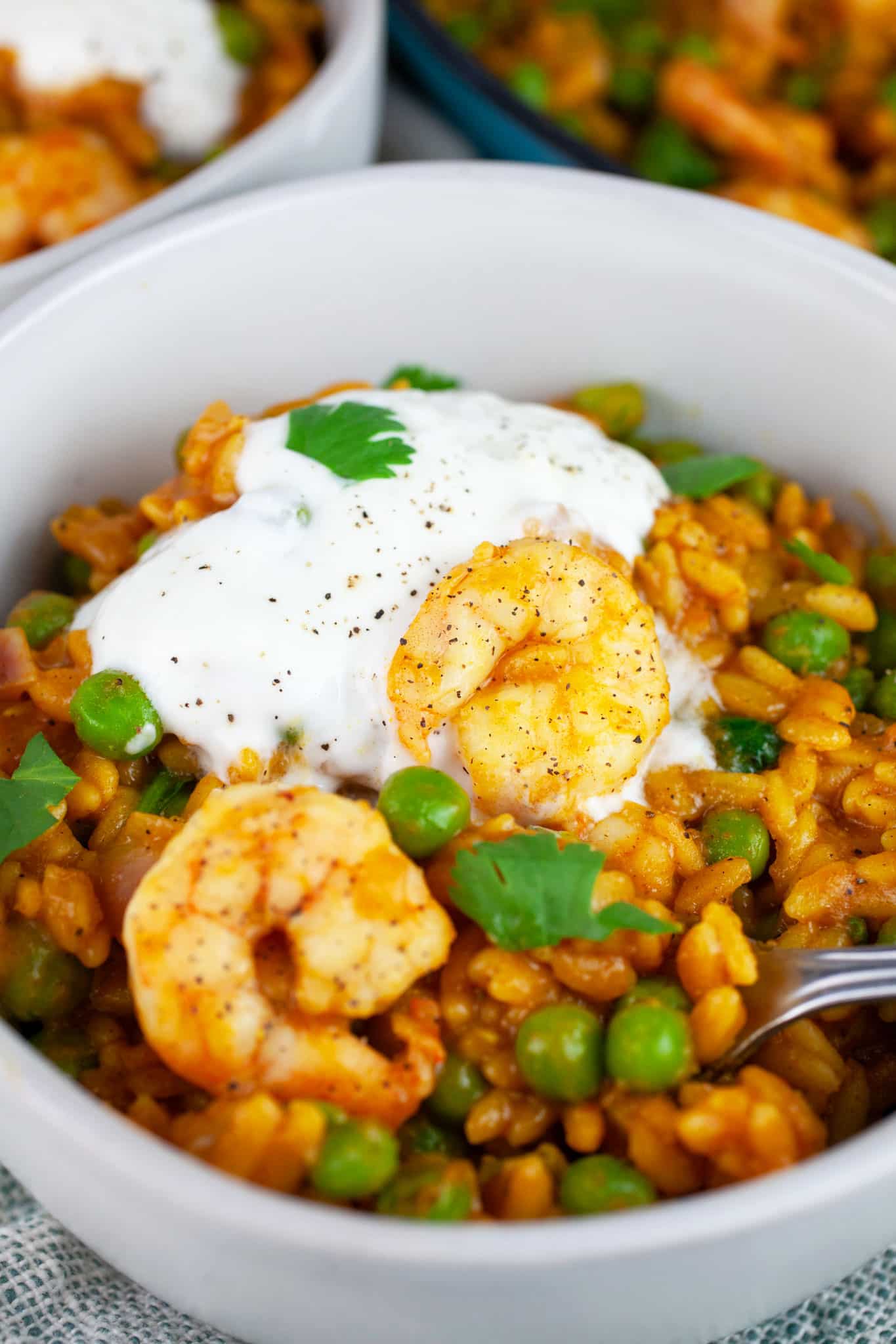 Curry orzo with peas, spinach, shrimp, Greek yogurt and cilantro in white bowl with fork.