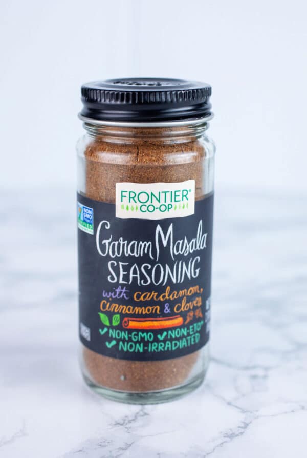 Unopened jar of garam masala on white surface.