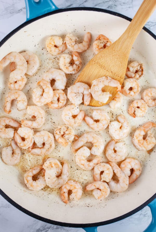 Shrimp sauteed in skillet with wooden spatula.