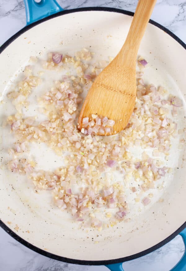 Minced garlic and shallots sauteed in skillet with wooden spatula.