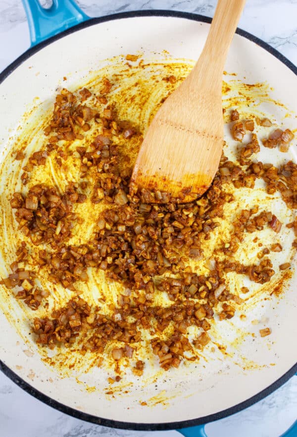 Garlic, shallots, and Indian spices sauteed in skillet with wooden spatula.