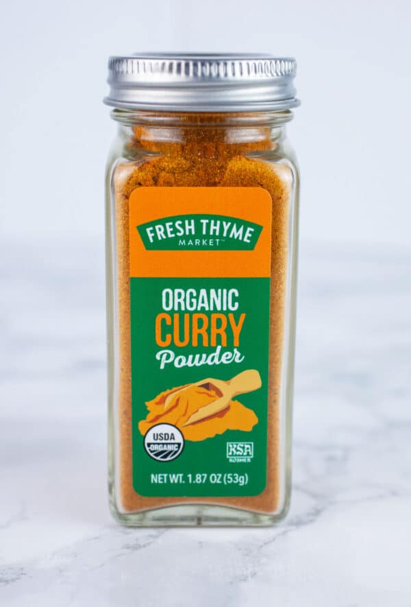 Unopened jar of curry powder on white surface.