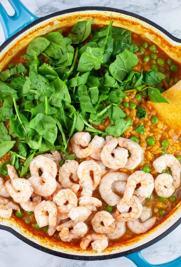 Orzo pasta, sauteed shrimp, and fresh spinach in skillet with wooden spatula.