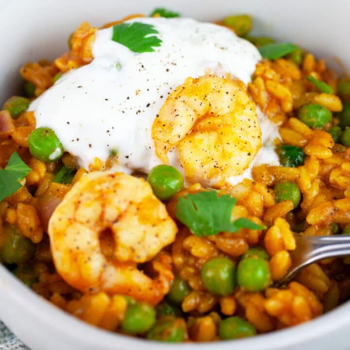 Curry orzo with peas, shrimp, and Greek yogurt garnished with fresh cilantro in white bowl with fork.