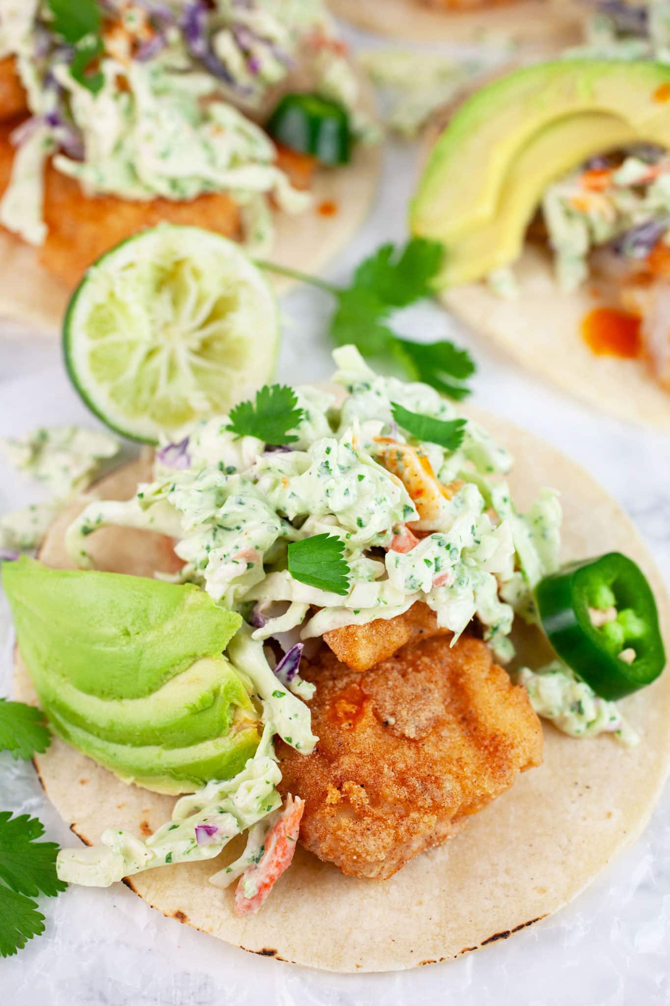 Fish tacos with cilantro lime coleslaw, avocado, jalapeno, cilantro, and limes on corn tortillas.