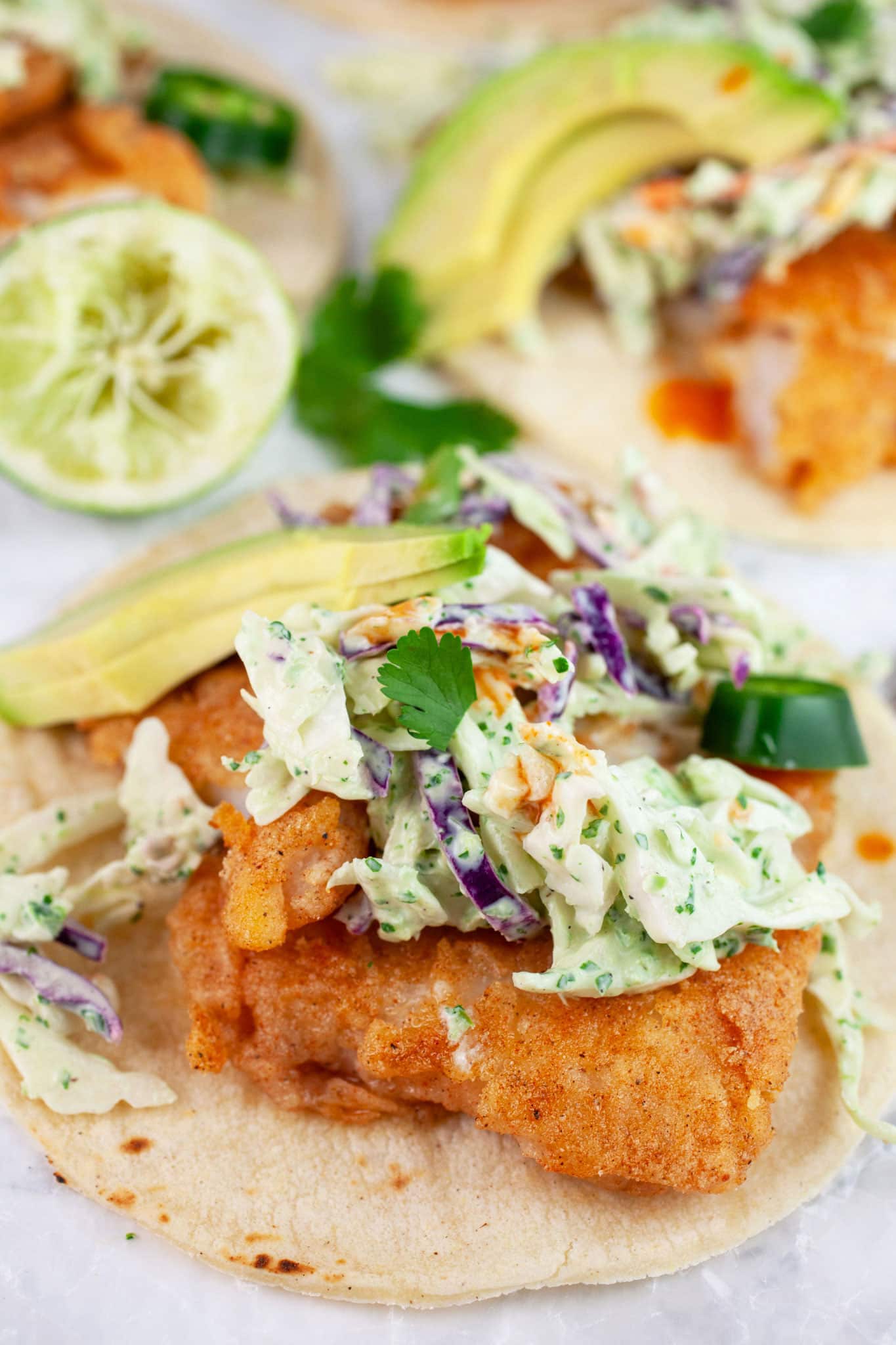 Fish tacos with cilantro lime slaw, sliced avocado, sliced jalapenos, and cilantro on corn tortillas.