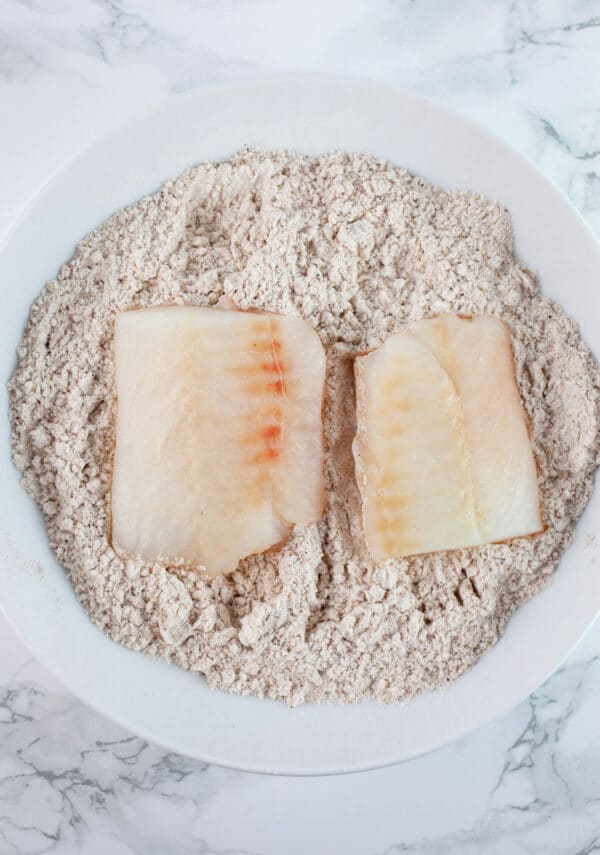 Seasoned gluten free flour blend with uncooked fish filets in white bowl.