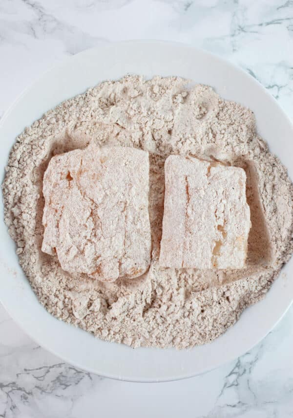 Fish filets coated in seasoned gluten free flour blend in white bowl.