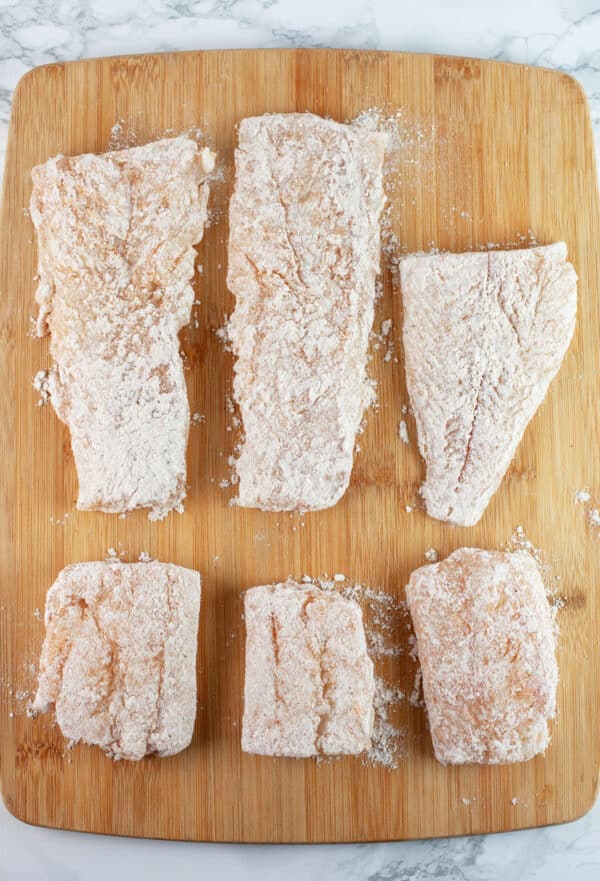 Uncooked fish filets coated in gluten free flour mixture on wooden cutting board.
