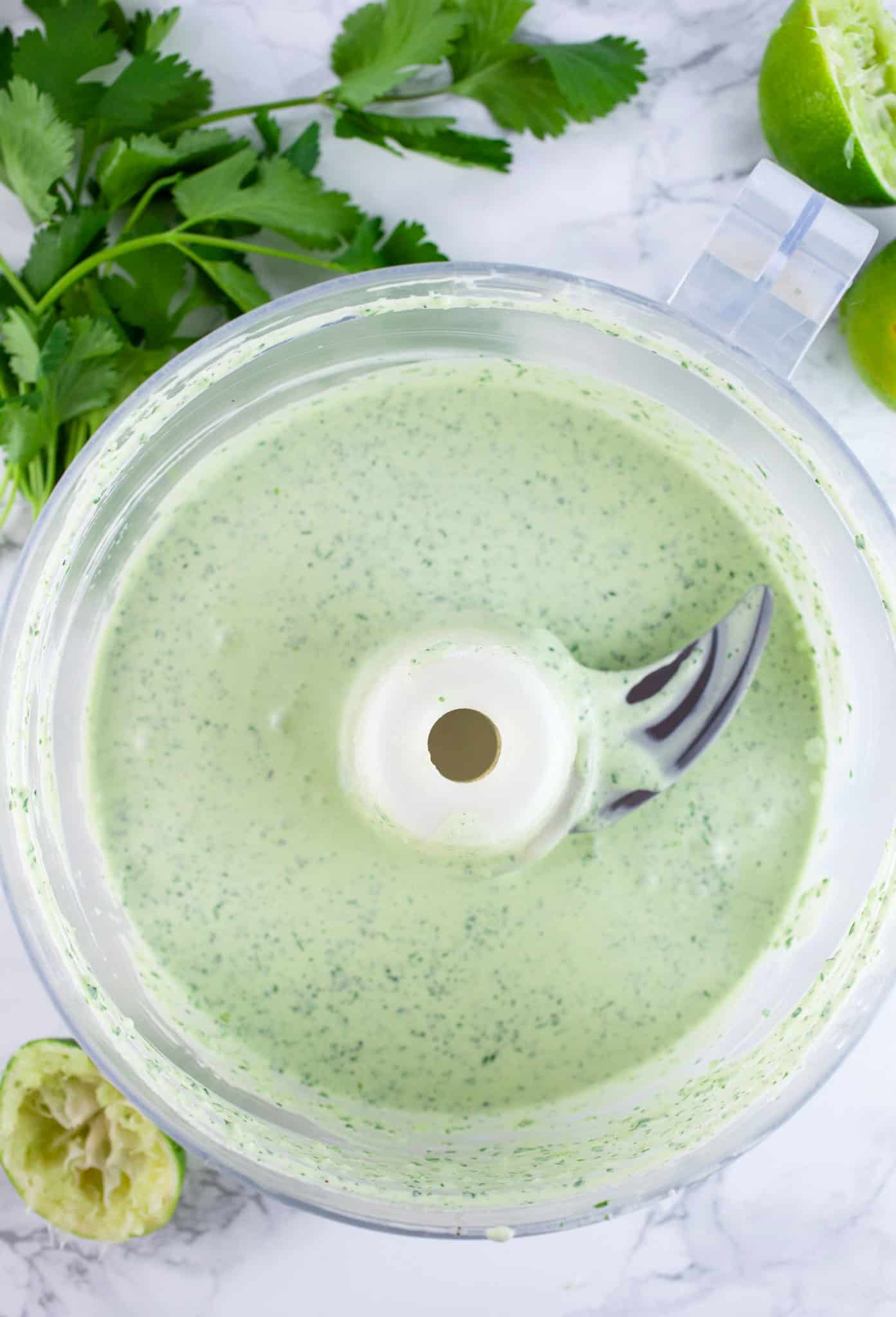 Coleslaw dressing in food processor next to fresh cilantro and squeezed limes.