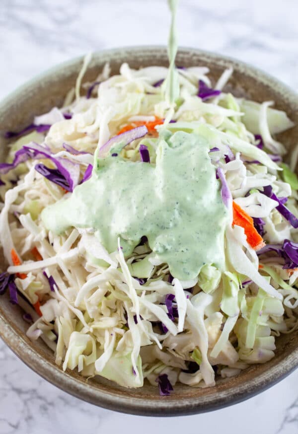 Coleslaw dressing poured onto shredded cabbage in ceramic bowl.