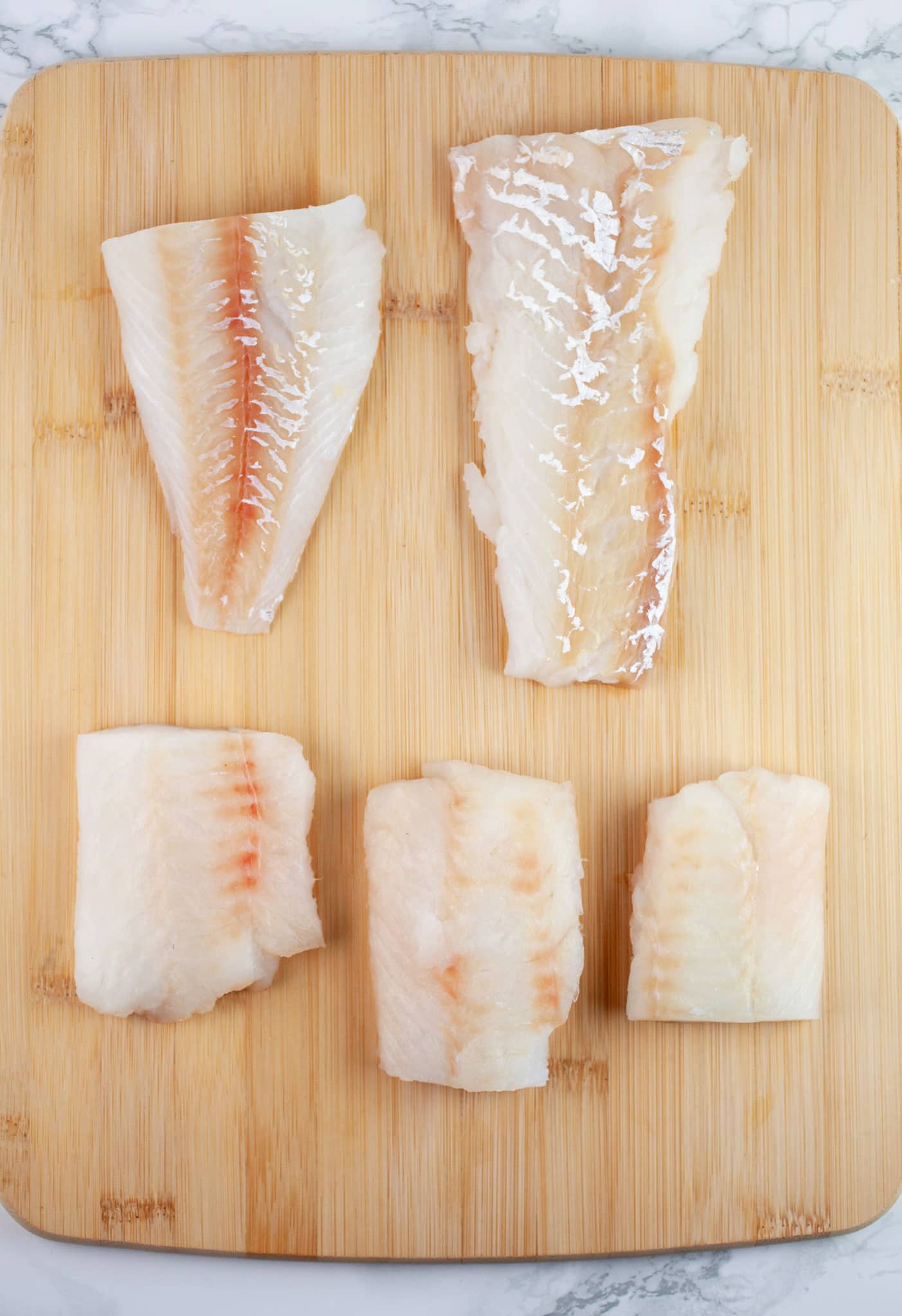 Raw cod fish filets on wooden cutting board.