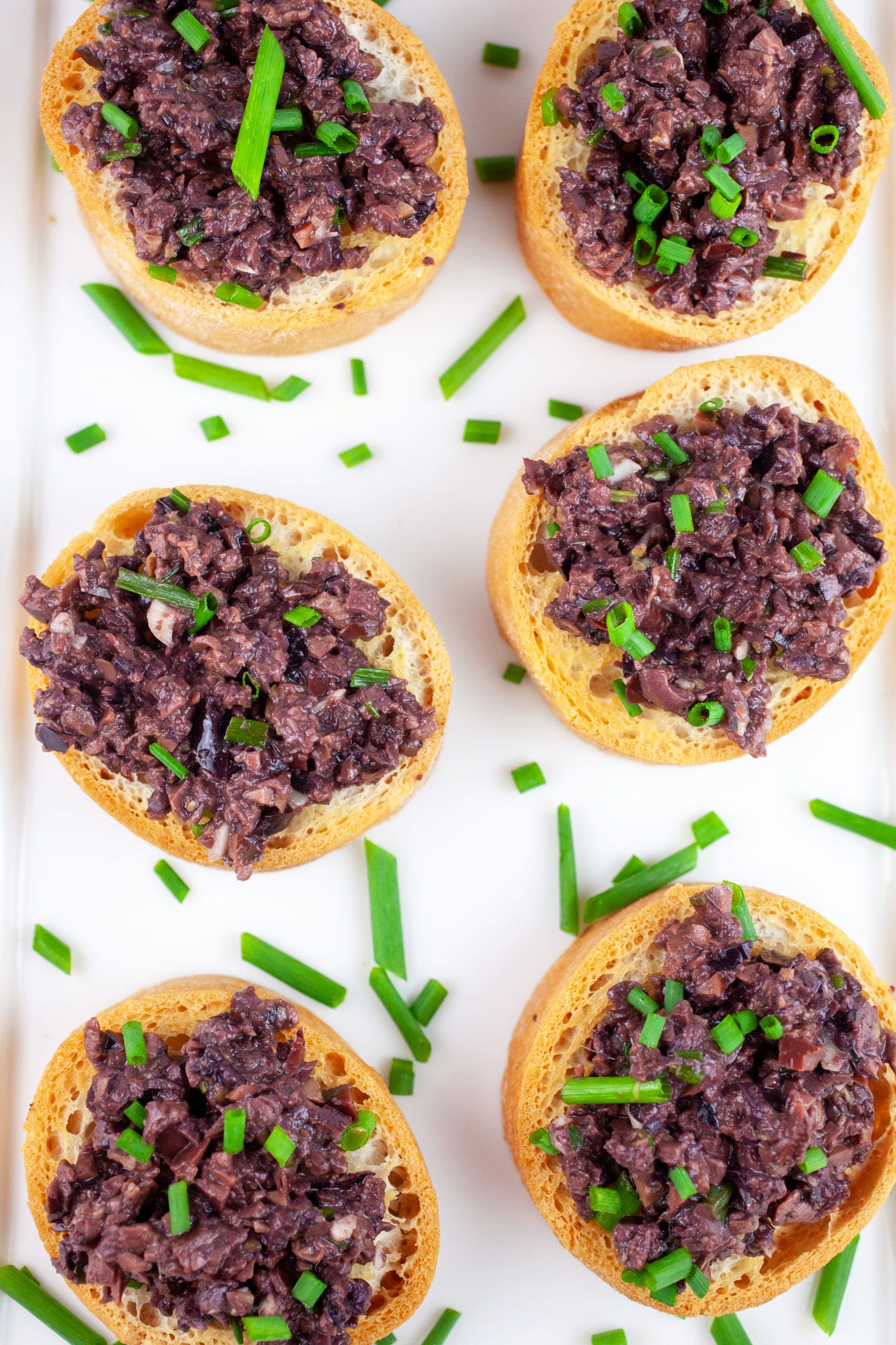 Kalamata olive tapenade on white serving platter garnished with minced chives.