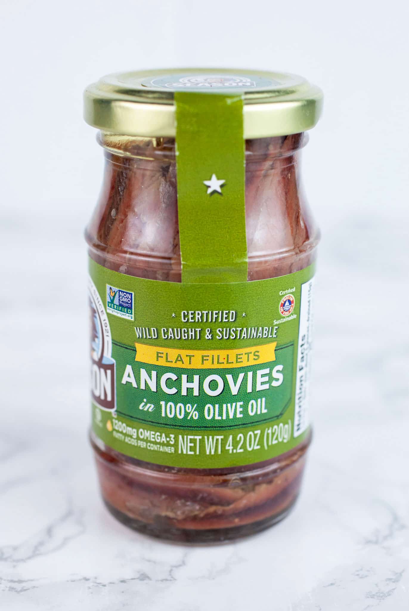 Unopened jar of anchovy filets on white surface.
