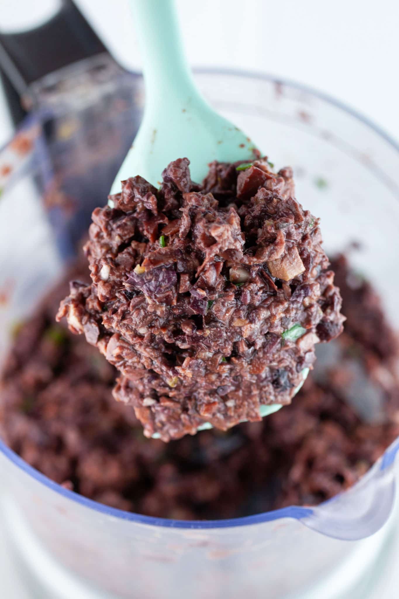 Kalamata olive tapenade lifted on spatula from food processor.