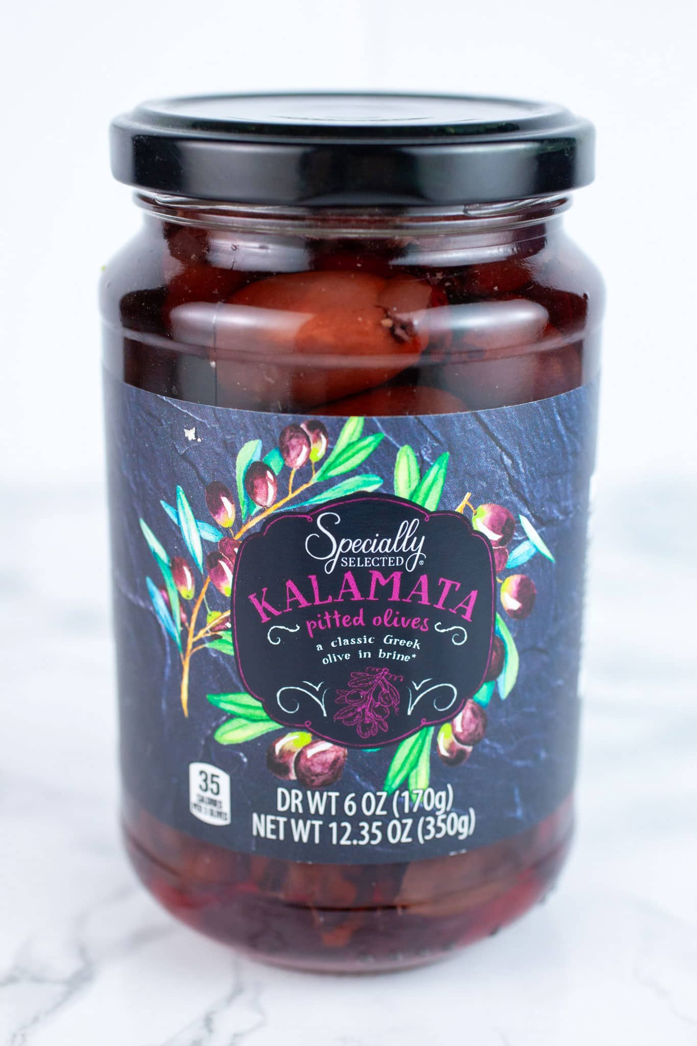 Unopened jar of kalamata olives on white surface.
